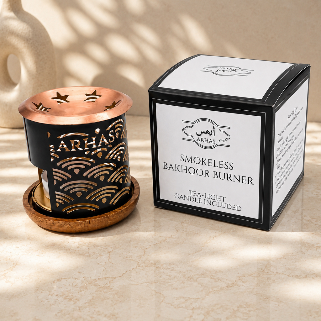 A black and copper Bakhoor burner set with a wooden base next to its white and black retail box, labeled 'Arhas Smokeless Bakhoor Burner'. The scene is styled on a beige marble surface with soft, dappled shadows.